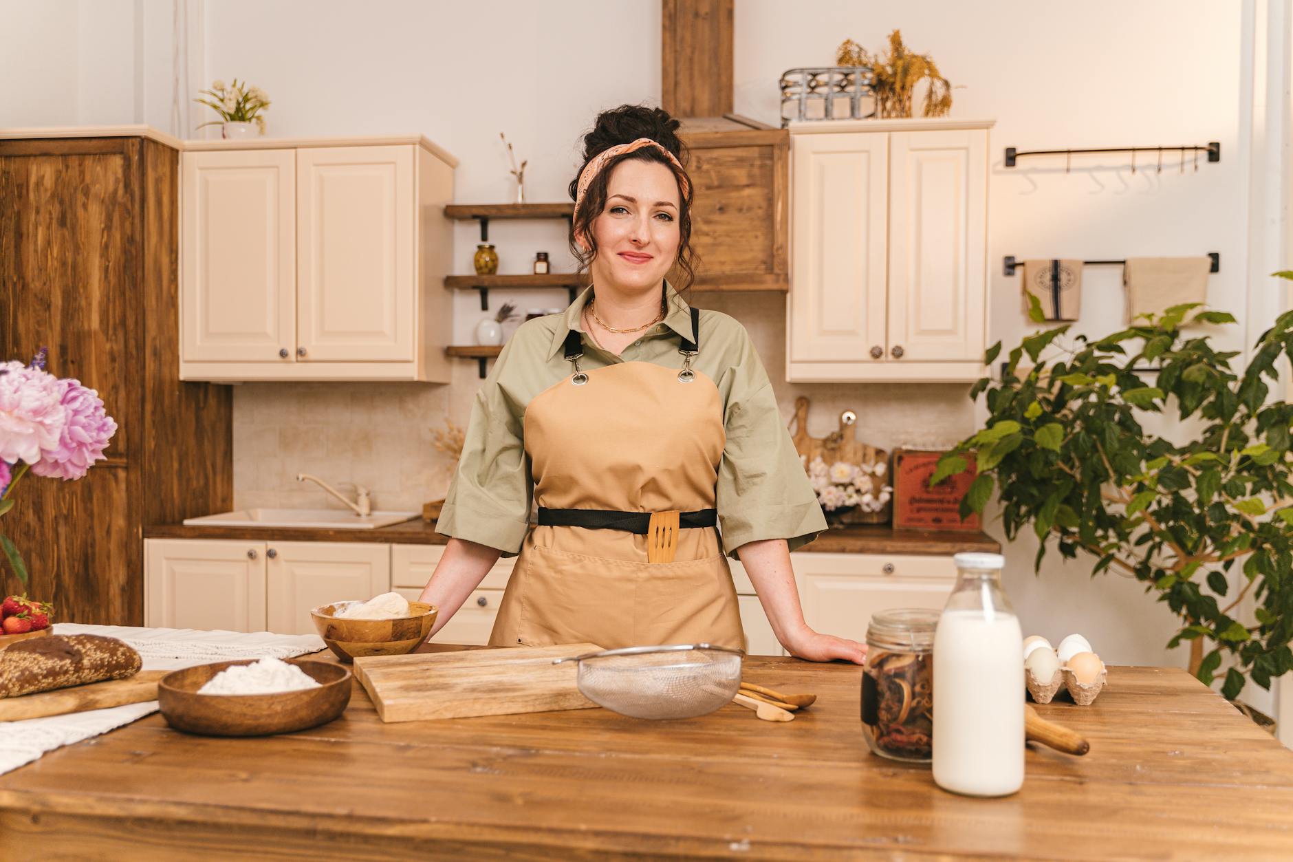 smiling woman in brown apron standing behind a wooden kitchen counter