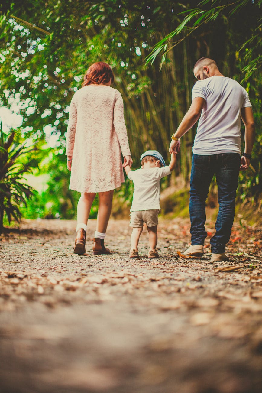 low angle shot of a child held by woman and man on on each hand walking on an unpaved pathway outdoors Blog Article Categories Parenting
