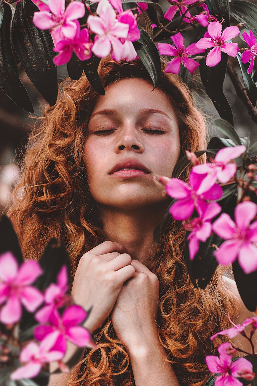 woman surrounded by pink petaled flowers Why Stress is Sabotaging Your Hair Health