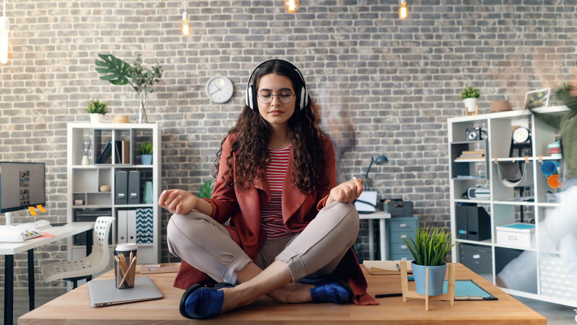 a woman sitting in meditation in a room with a laptop