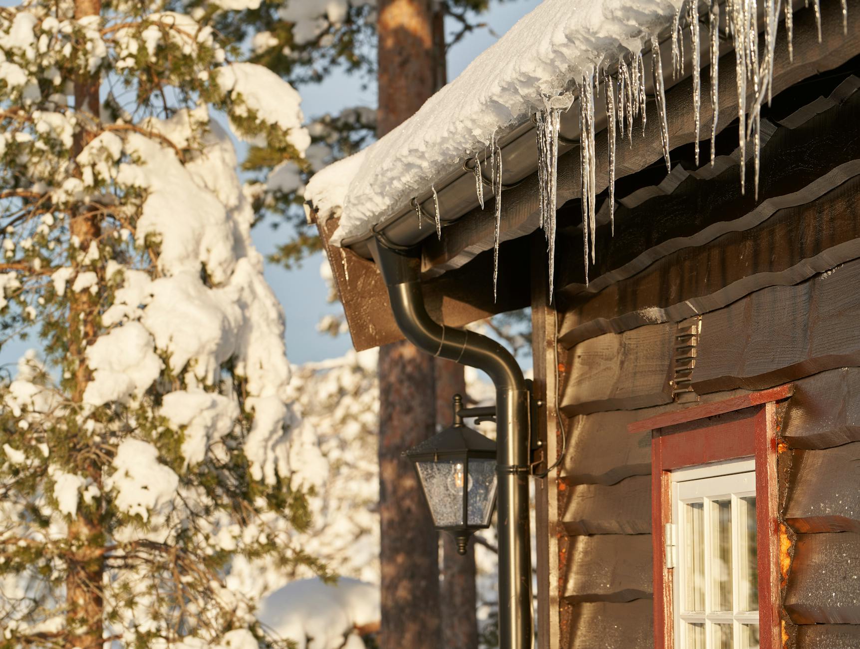 close up of icicles on old wooden house in winter gutter maintenance
