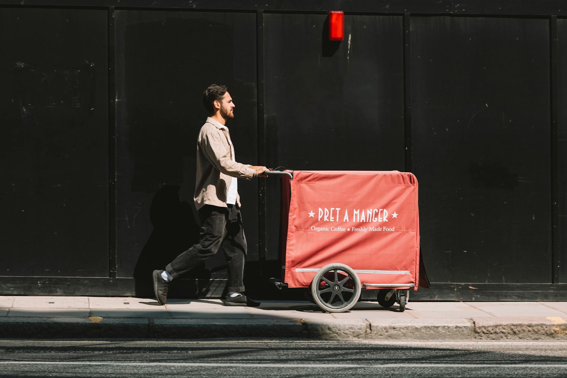 man on a street pushing a red cart against a black wall 3 Reasons to Start a Coffee Cart