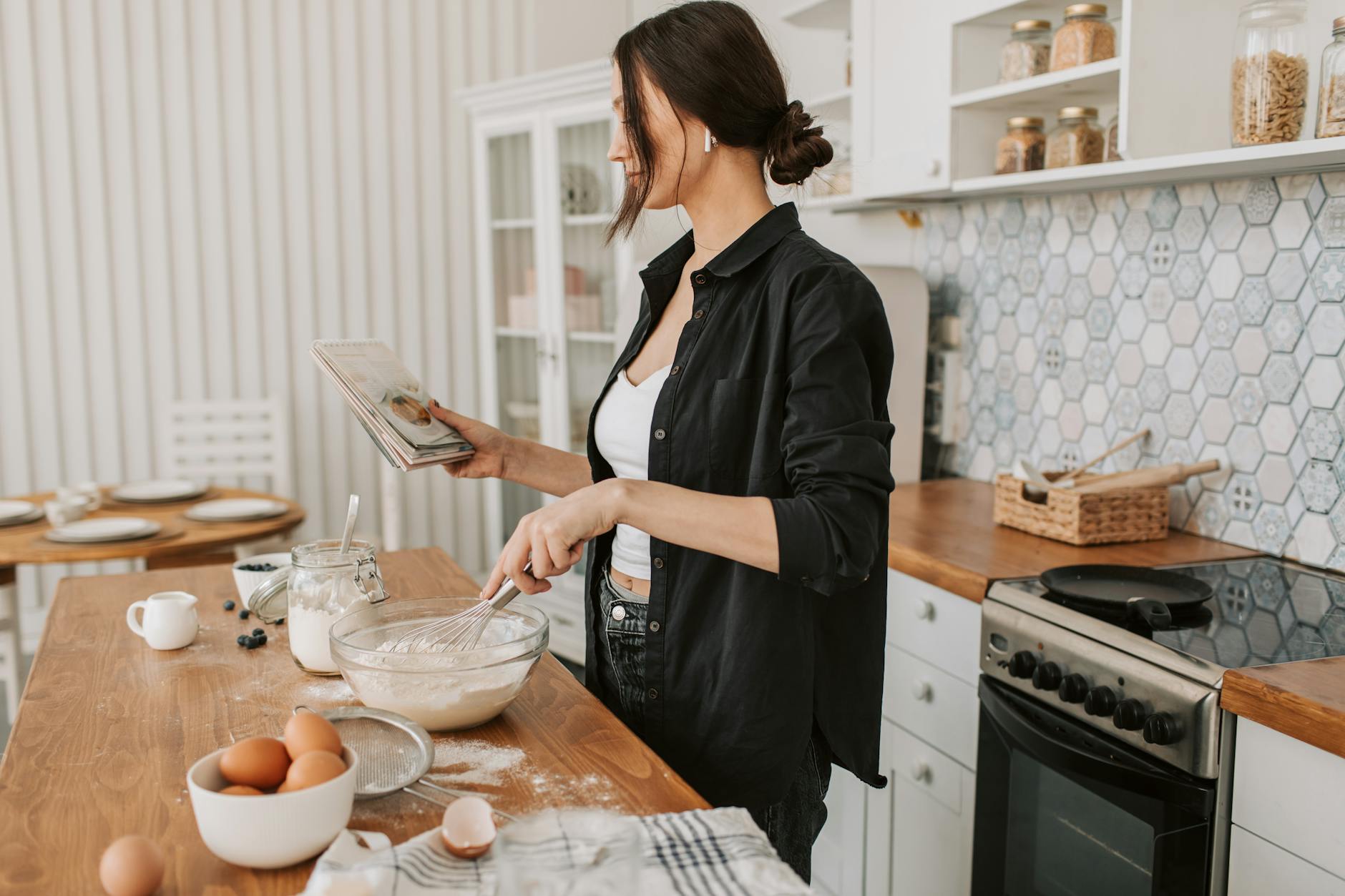 woman in black long sleeves holding a recipe book while cooking How to Set Up a Kitchen From Scratch: STR Hosts & New Homeowners