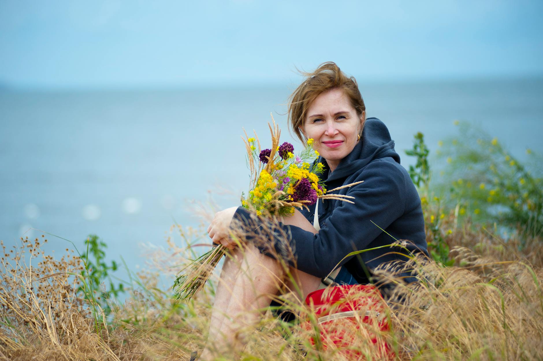 woman sitting on grass holding flowers wearing black hoodie