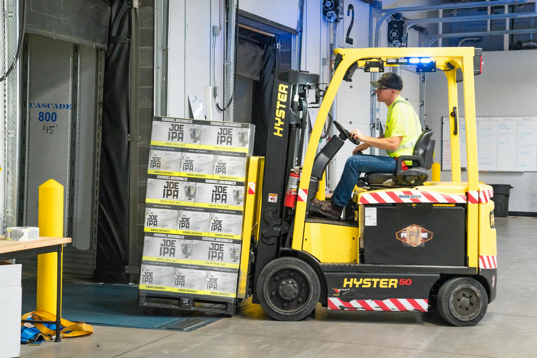 man riding a yellow forklift lifting boxes What Businesses Need to Know About Driver Safety Compliance