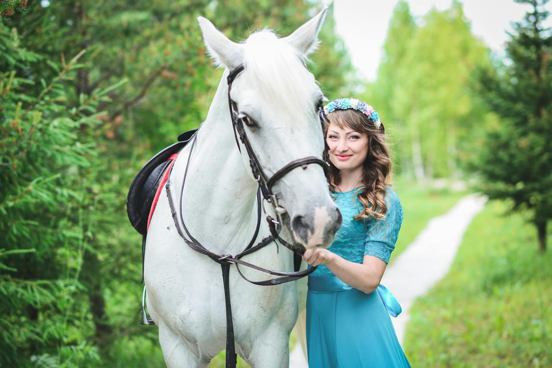 smiling woman in blue dress standing beside white horse
