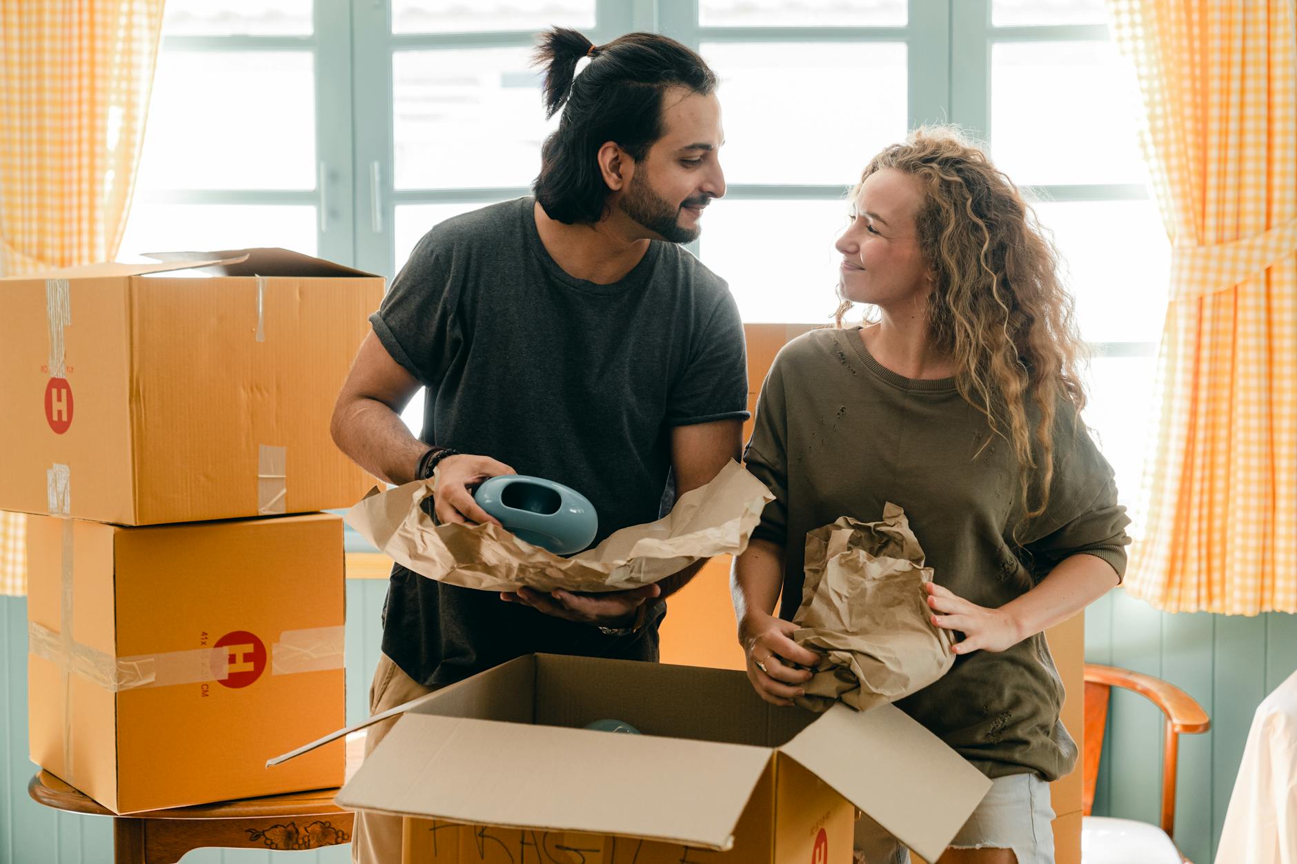 multiethnic couple packing ceramic belongings in parchment before relocation The Family Guide to Moving During Big Life Changes