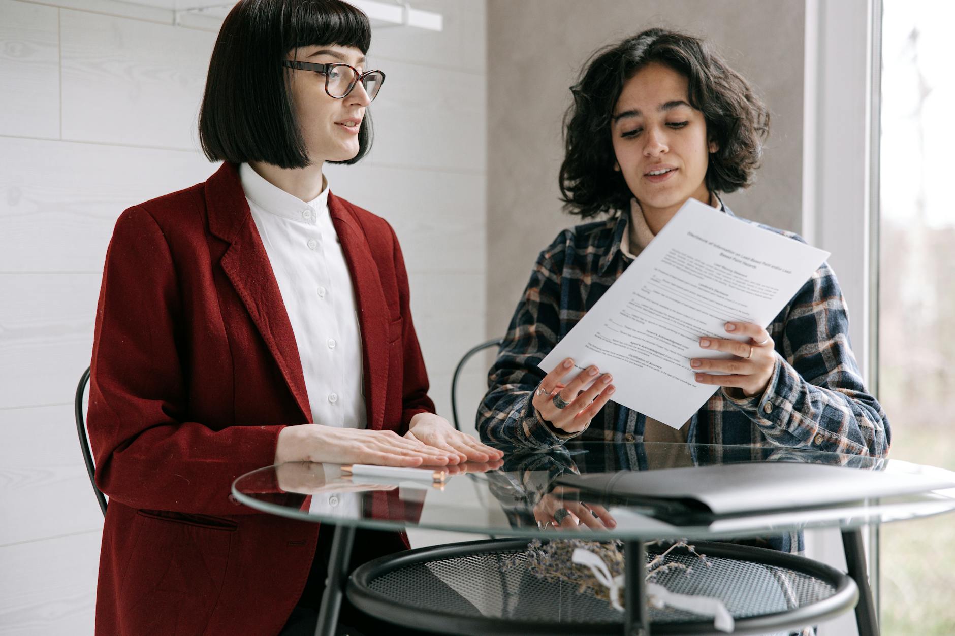 woman in blue button up plaid shirt holding documents beside woman in red blazer Selling a House Fast Doesn’t Have to Be Stressful