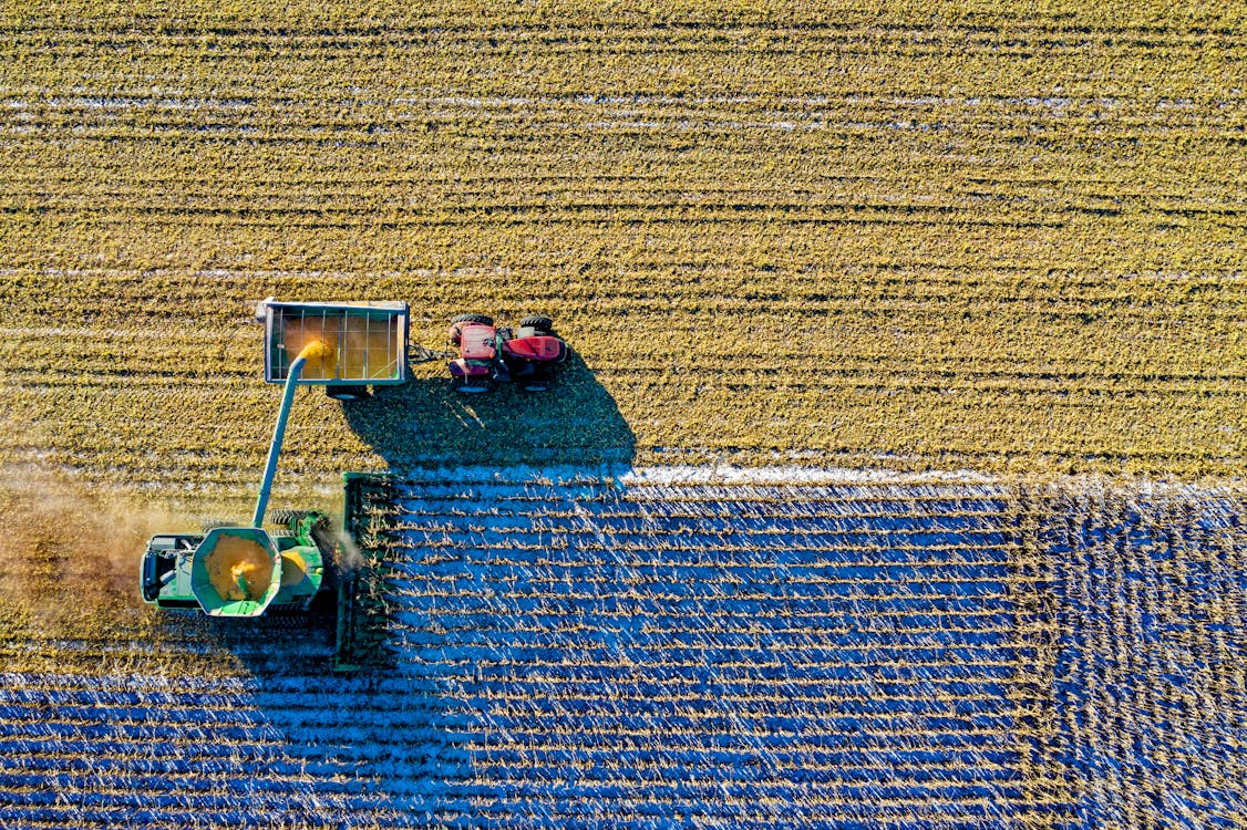 Aerial view of a green harvesting machine in a field, unloading crops into a attached trailer. Nearby, a red tractor is parked on the edge of the field. 9 Tips to Plan Ahead for the Next Farming Season