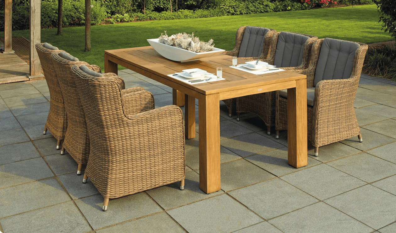 Outdoor dining set featuring a wooden table with a decorative centerpiece and cushioned wicker chairs, set on a tiled patio surrounded by a green lawn. Spring Garden Prep Guide: Simple Upgrades with Big Impact