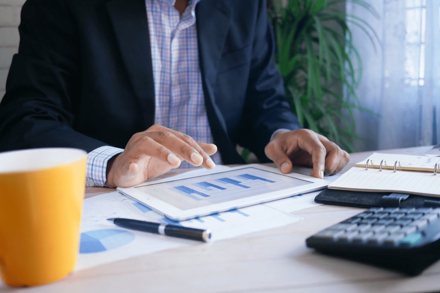 7 Simple Steps to Build Financial Security in Uncertain Times 7 A person in a suit using a tablet to analyze financial data, with a coffee cup and notebook on a desk.