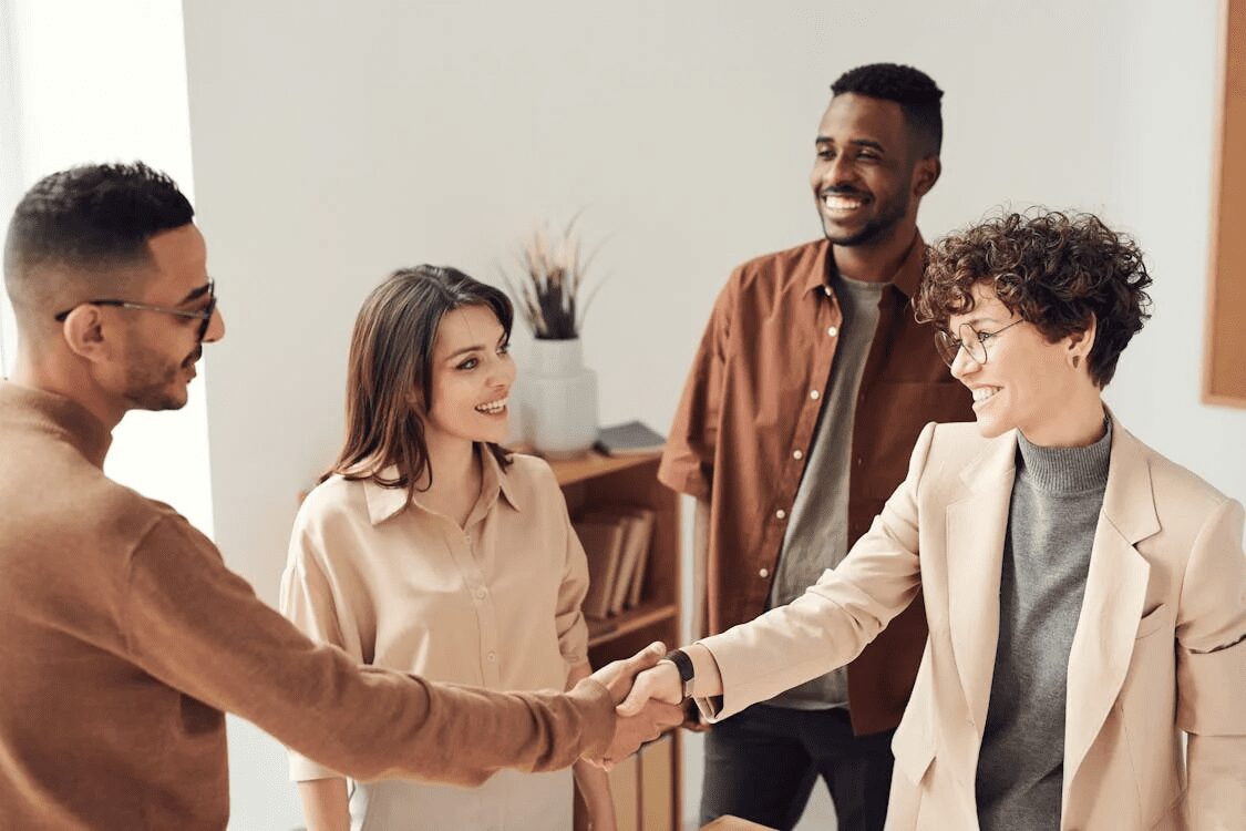 10 Time-Saving Tricks to Improve Customer Service 7 Four professionals engaging in a friendly handshake and conversation in an office setting. 10 Time-Saving Tricks to Improve Customer Service