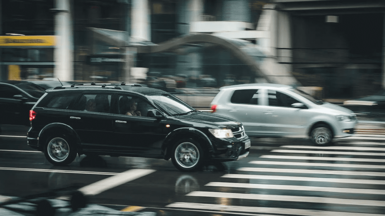 A black SUV and a grey car crossing a crosswalk during the daytime, with a busy urban background. How to Protect Yourself After a Hit-and-Run