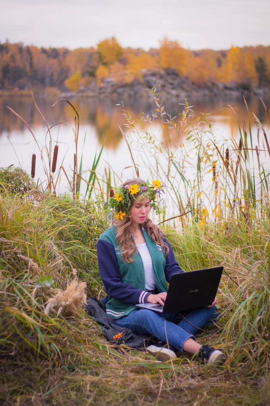 woman in jacket sitting on green grass field while using black laptop Rural Tech Tools That Make Country Living Easier