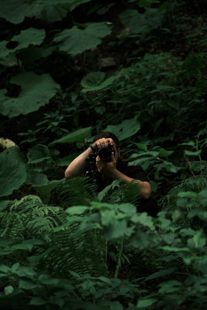 a man taking a photo inside of the big leaves in a jungle The Rise of Practical Smart Gear for Tactical Tech at Home