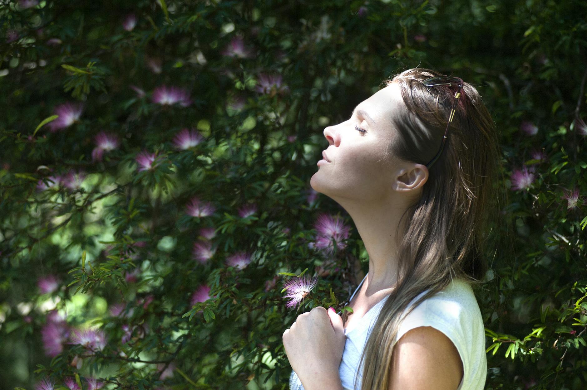 woman closing her eyes against sun light standing near purple petaled flower plant The Hidden Struggle of High-Achieving Women: Mental Burnout