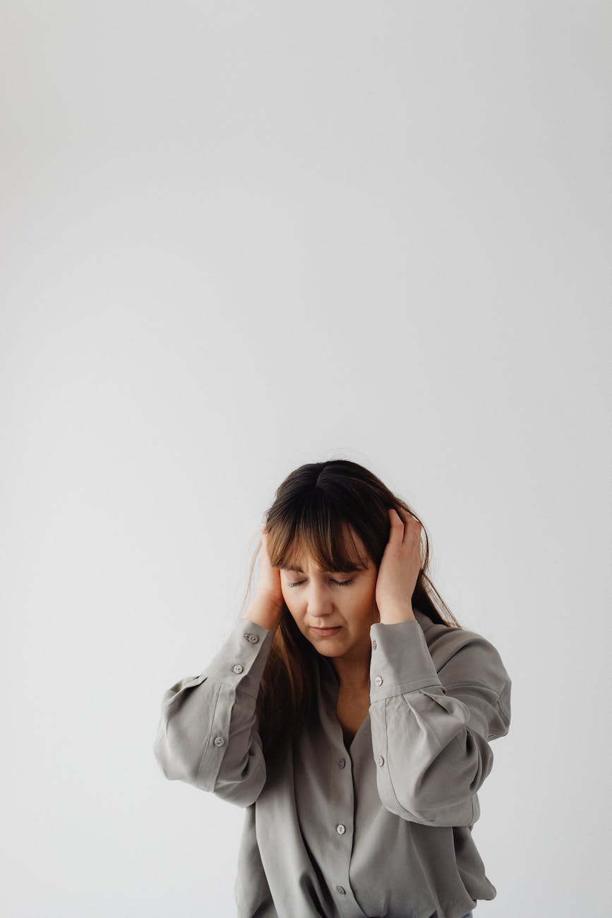 woman in gray long sleeves with eyes closed and hands on her ears Living With Tinnitus: How to Cope With Ringing in the Ears
