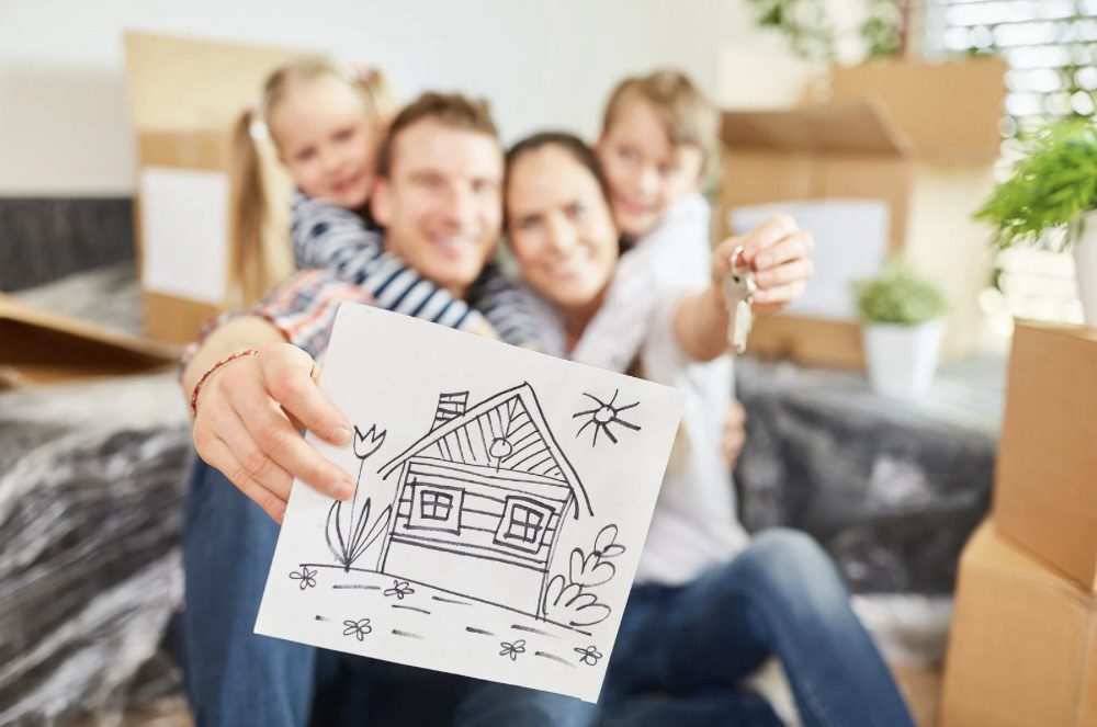 Is Building Your Own Home the Ultimate Dream or a Costly Mistake? 13 A happy family with two children is sitting in their new living room surrounded by moving boxes. The father holds up a drawing of a house while the mother shows a set of keys. Is Building Your Own Home the Ultimate Dream or a Costly Mistake?