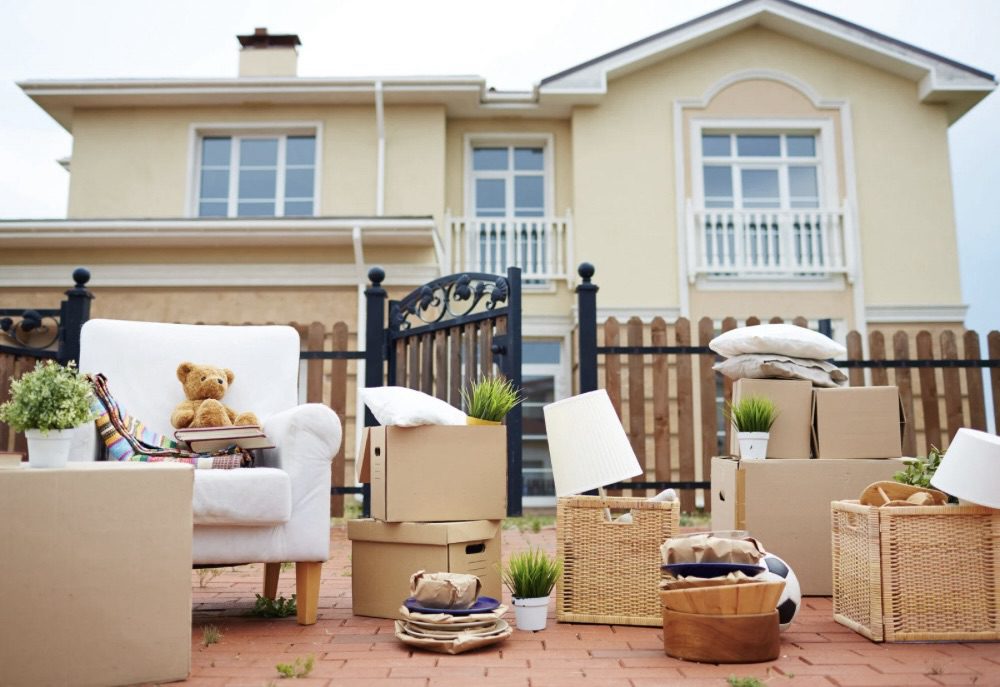 A white armchair with a teddy bear and plant sits in front of a house, surrounded by moving boxes and other items like pillows and baskets. Relocating for Work: 6 Smart Strategies for a Smooth Move