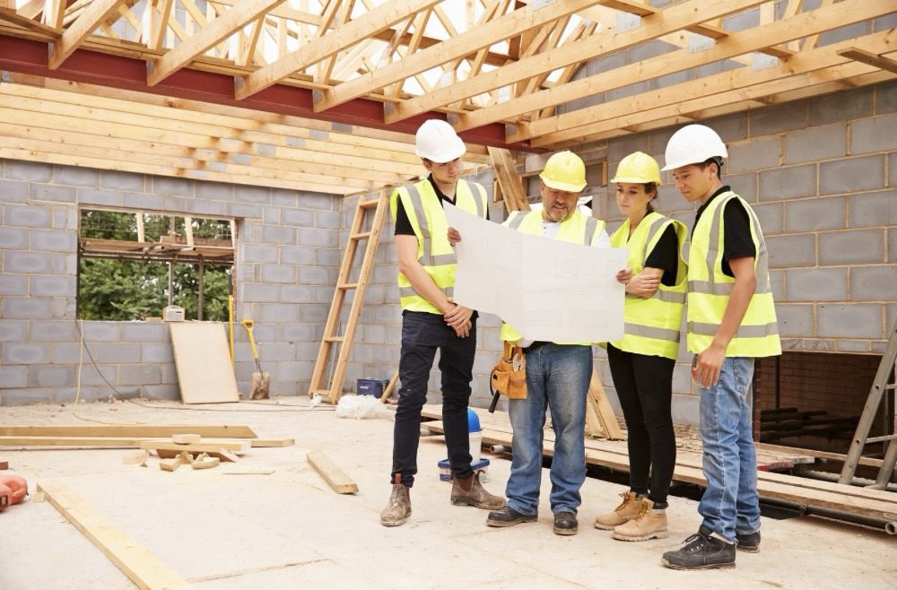 Is Building Your Own Home the Ultimate Dream or a Costly Mistake? 10 A group of construction workers examining blueprints at a building site, surrounded by wooden beams and unfinished walls. Is Building Your Own Home the Ultimate Dream or a Costly Mistake?