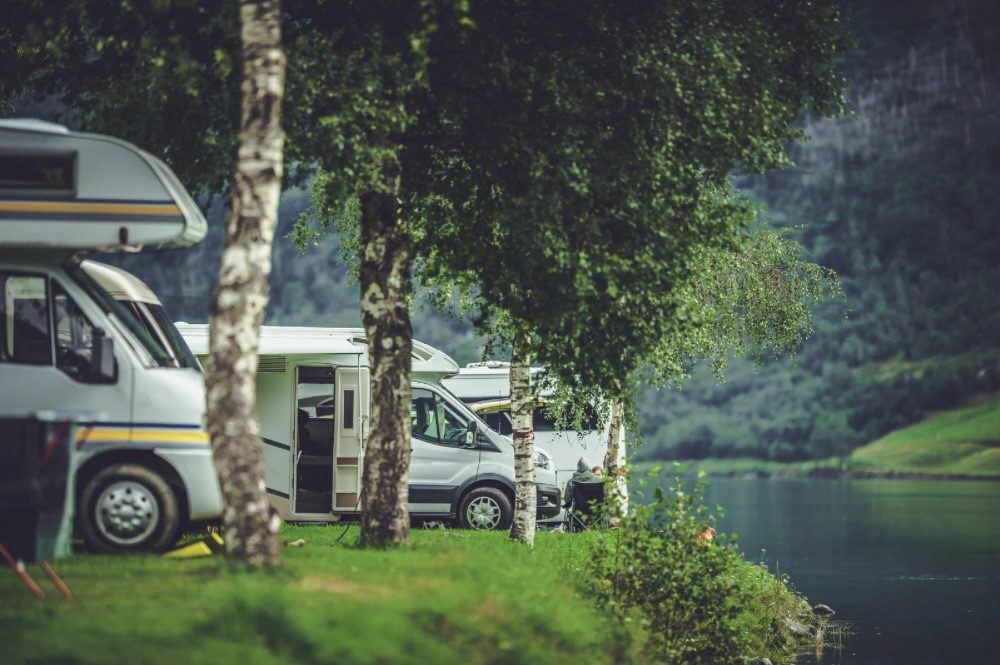 Row of RVs parked by a serene lake surrounded by lush greenery. Road Trip Tips for Comfort and Adventure