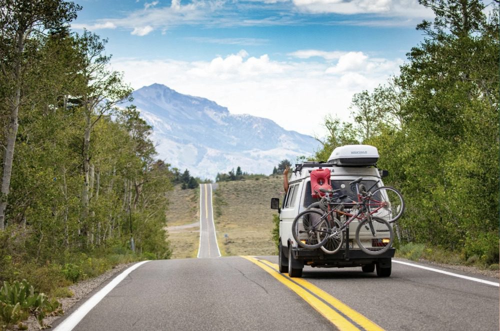 A camper van driving down a winding road surrounded by trees and mountains in the background. Road Trip Tips for Comfort and Adventure