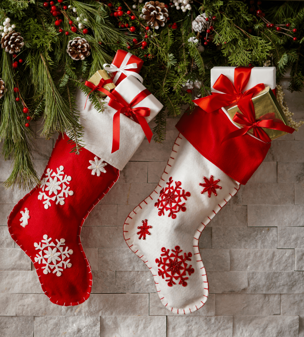 Two festive Christmas stockings hanging from a garland, one red and one white, both adorned with snowflake designs and topped with wrapped gifts tied with ribbons. 100+ Eco-Friendly Stocking Stuffer Ideas for the Whole Family