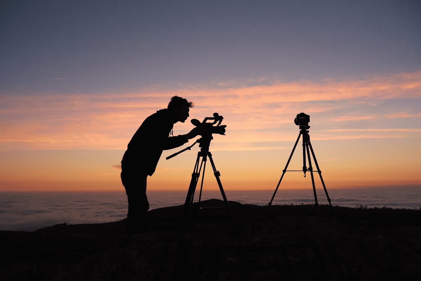 6 Careers That Let You Travel and Work At The Same Time 9 Silhouette of a person adjusting a camera on a tripod during sunset, with another tripod in the background. 6 Careers That Let You Travel and Work At The Same Time