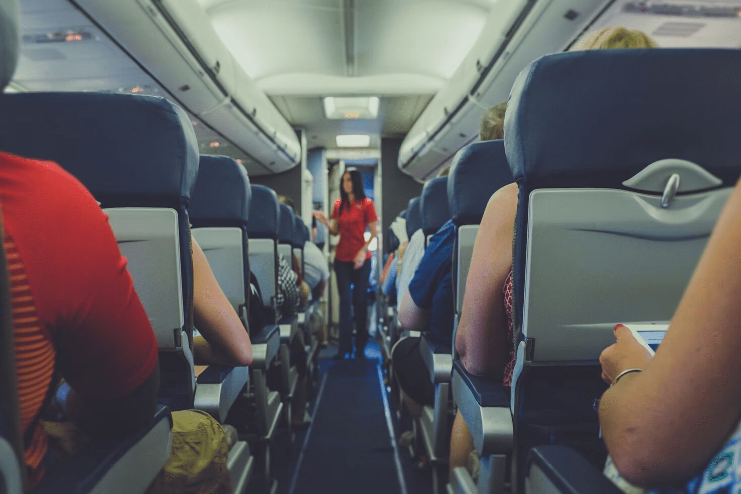 6 Careers That Let You Travel and Work At The Same Time 7 Interior view of an airplane with passengers seated and a flight attendant in red uniform walking down the aisle. 6 Careers That Let You Travel and Work At The Same Time