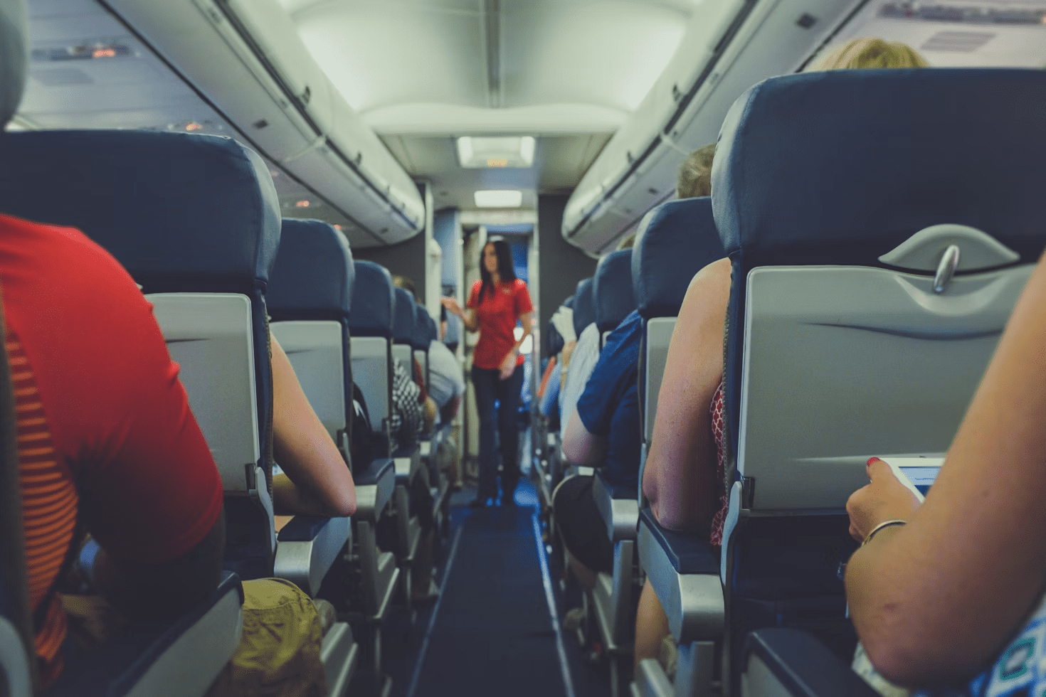 6 Careers That Let You Travel and Work At The Same Time 7 Interior view of an airplane with passengers seated and a flight attendant in red uniform walking down the aisle. 6 Careers That Let You Travel and Work At The Same Time