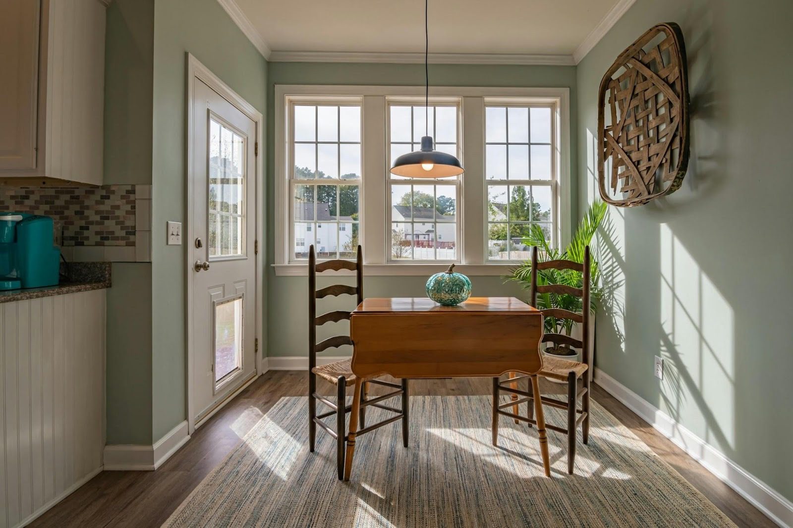 A cozy dining area with a wooden table and two chairs, located in a well-lit room with green walls and large windows, showing a bright atmosphere. The Truth About Real Estate Investing: Profit, Pitfalls, and Smart Strategies