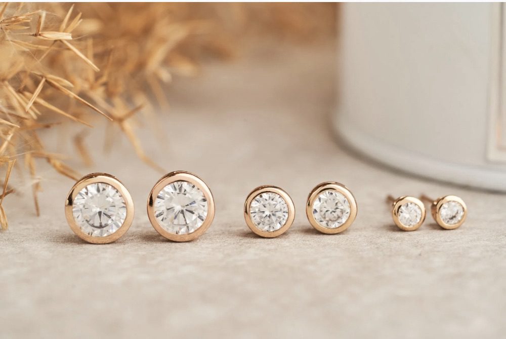 A collection of diamond gold stud earrings in different sizes and settings, displayed on a neutral background with hay. Best Diamond Gold Stud Earrings for Women