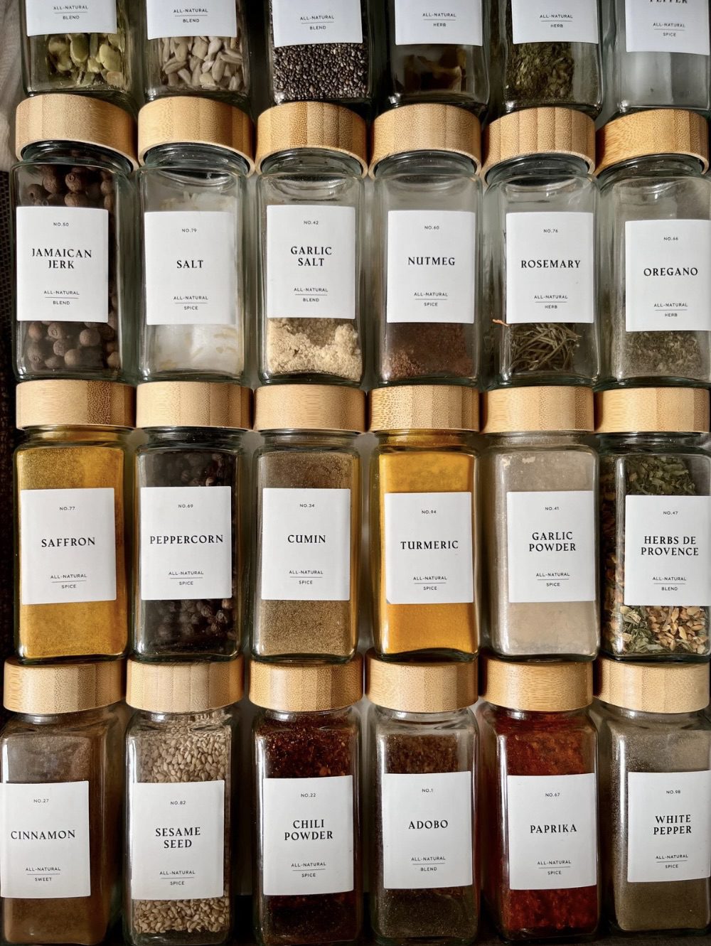 A neatly organized variety of spice jars on shelves, each labeled with its contents and description, showcasing an array of herbs and spices. 30 Essential Winter Pantry Staples for a Self-Sufficient Kitchen