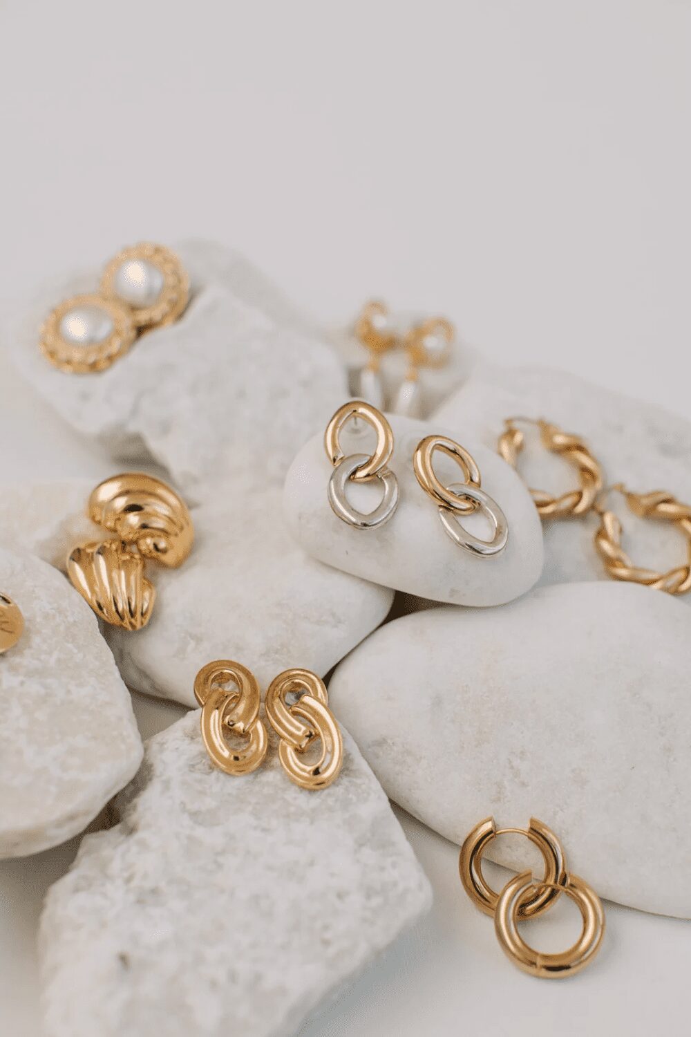 A collection of various gold earrings displayed on white stones, featuring different designs including pearl studs, twisted hoops, and linked styles. Best Diamond Gold Stud Earrings for Women