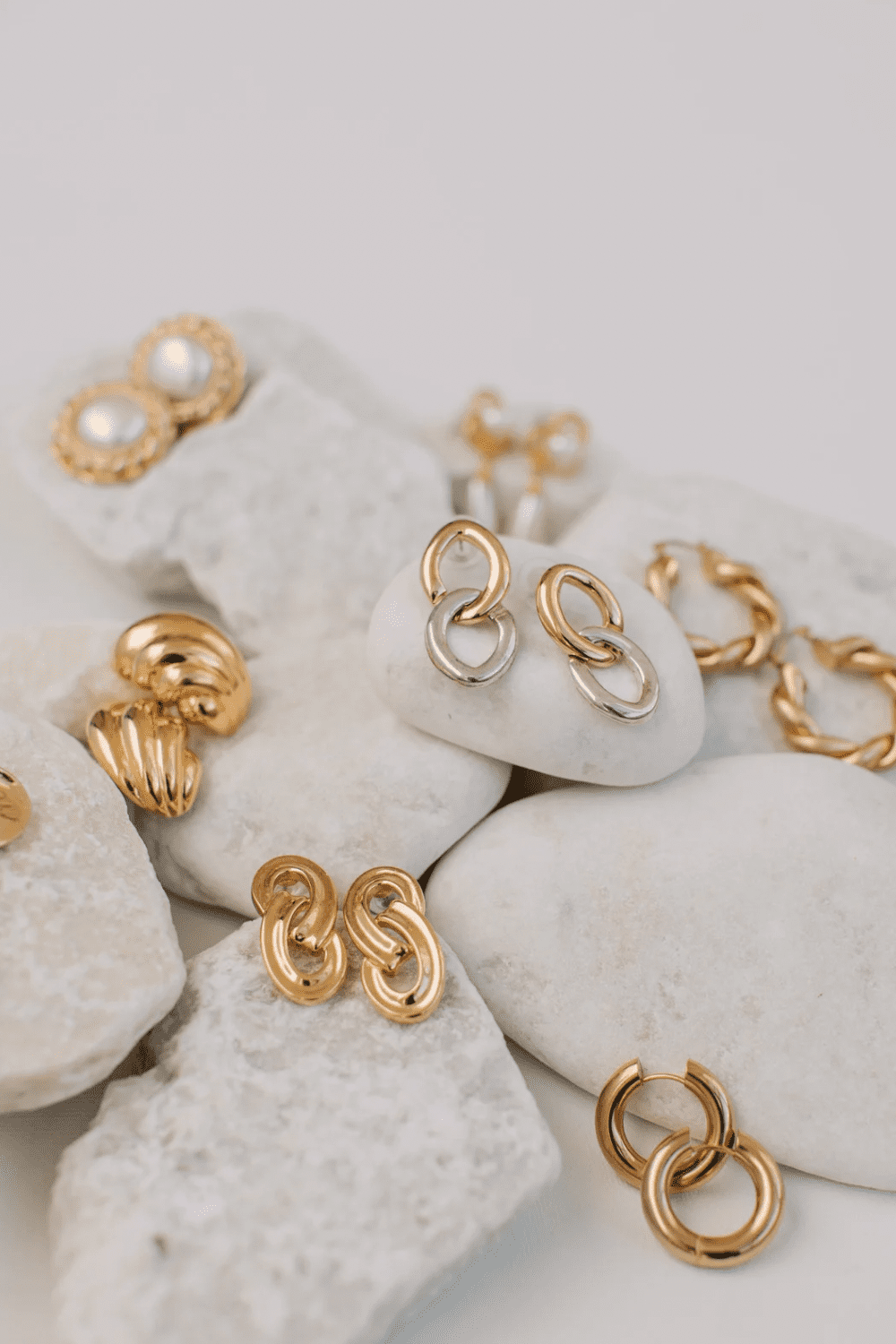 A collection of various gold earrings displayed on white stones, featuring different designs including pearl studs, twisted hoops, and linked styles. Best Diamond Gold Stud Earrings for Women