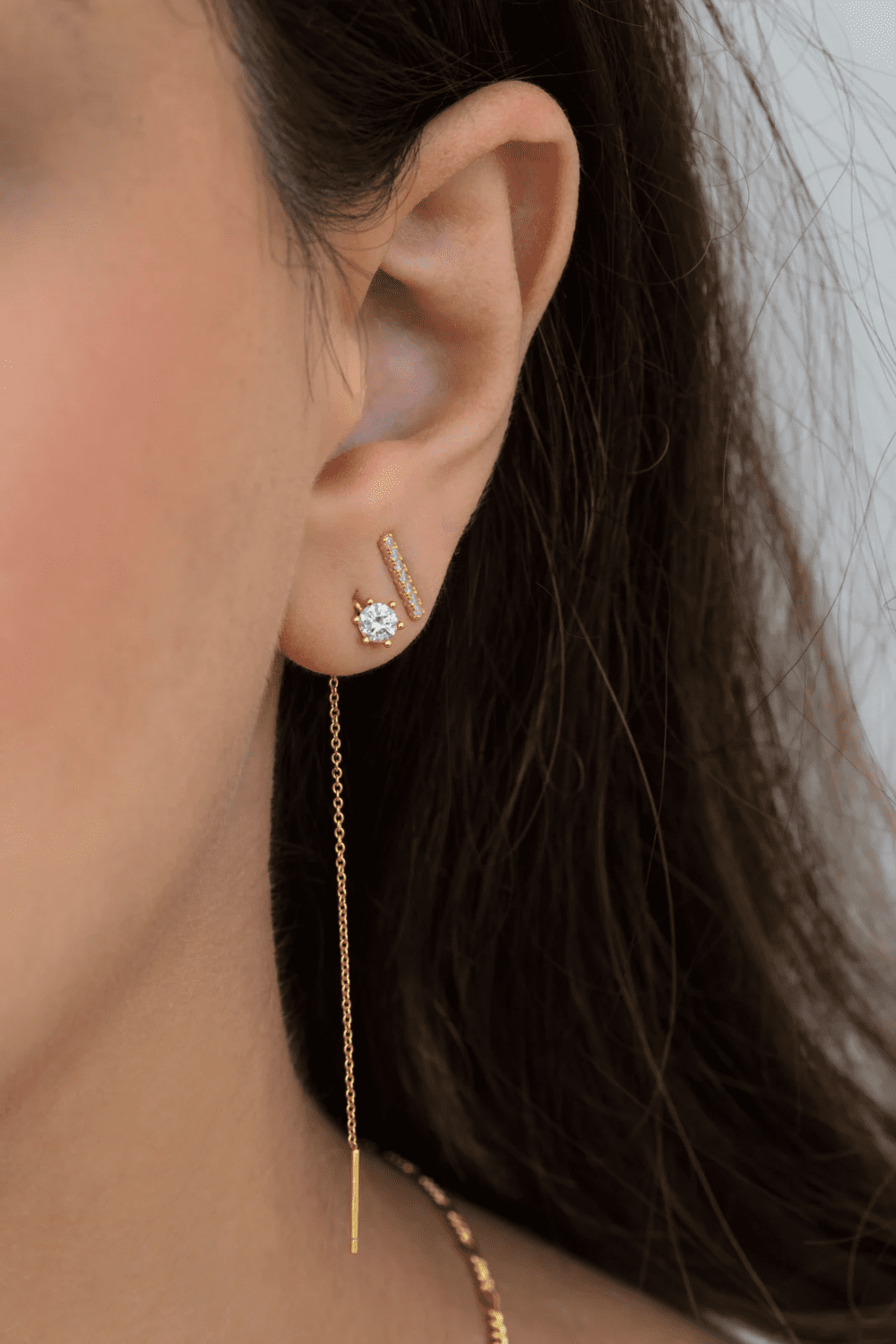 Close-up of a woman's ear featuring diamond gold stud earrings and a delicate chain earring, showcasing a modern and elegant jewelry style. Best Diamond Gold Stud Earrings for Women