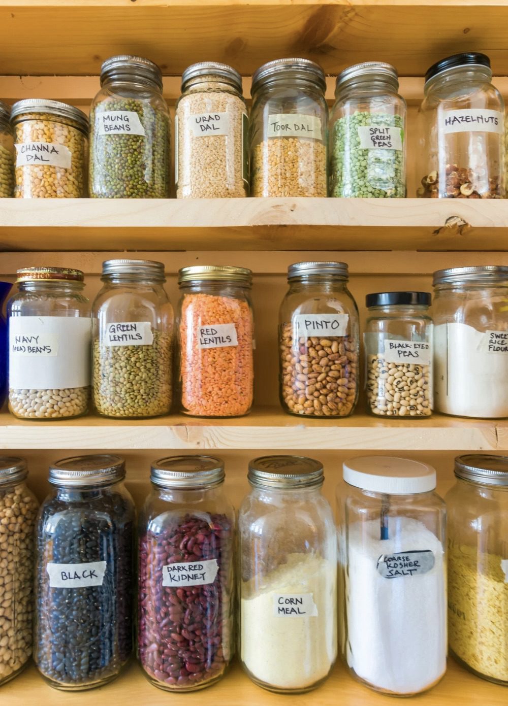 Shelves filled with labeled jars containing various legumes, lentils, and dry goods such as cornmeal and salt. 30 Essential Winter Pantry Staples for a Self-Sufficient Kitchen