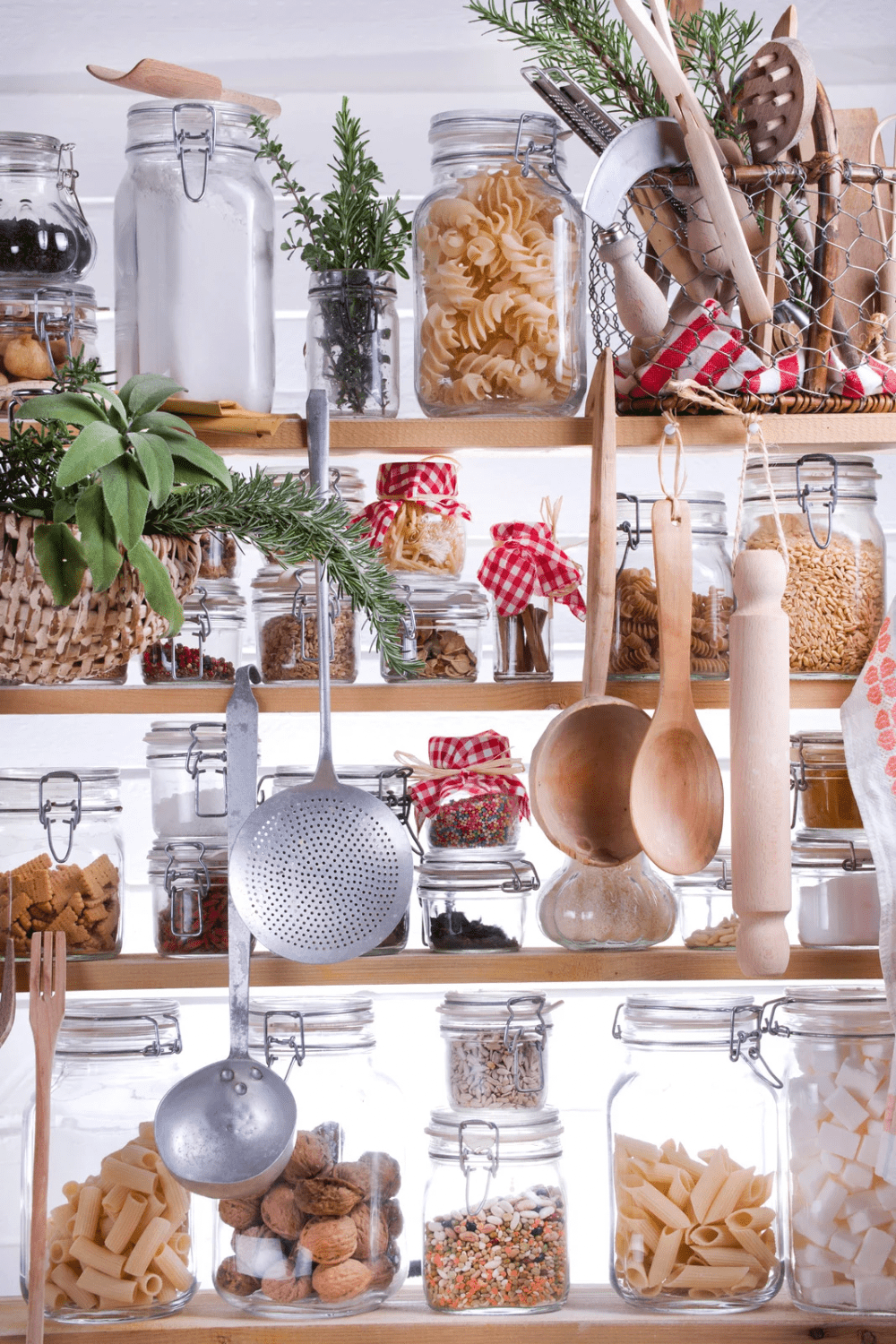 A beautifully organized pantry shelf featuring various jars filled with ingredients like pasta, nuts, and spices, alongside herbs and cooking utensils. 30 Essential Winter Pantry Staples for a Self-Sufficient Kitchen