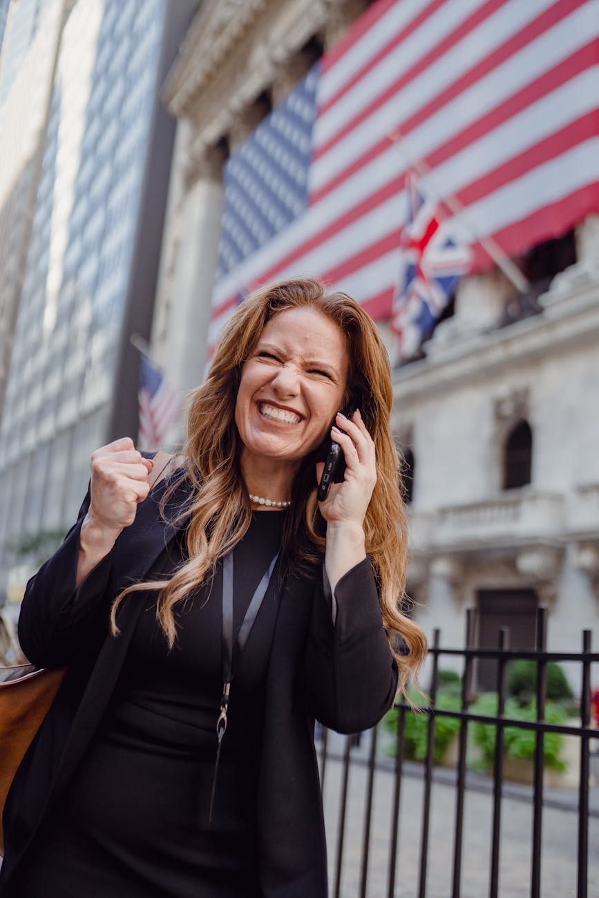 Best Airlines to Fly Business Class to the UK from the USA (2026 Guide) 7 excited woman using mobile phone on a street and us flag in background Best Airlines to Fly Business Class to the UK from the USA (2026 Guide)